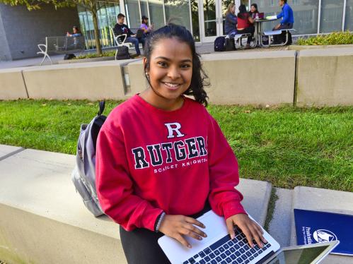 A young student works on a laptop while sitting outside