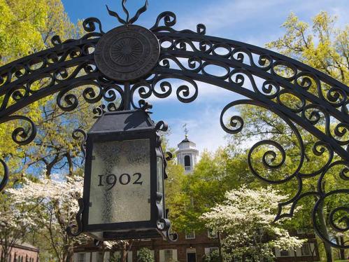 Gate on the Rutgers campus with the year 1902. The background is a clear summer sky with bright green trees.